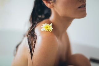 Woman in a bath with wet hair and a yellow flower on her shoulder, evoking calm, self-care, and natural beauty