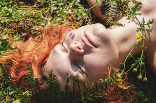 Woman with red hair relaxing among ferns and wildflowers in summer nature