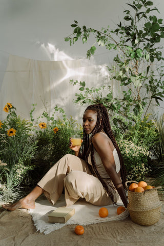 A woman sits peacefully on a soft white blanket in a sunlit garden surrounded by vibrant greenery and yellow sunflowers