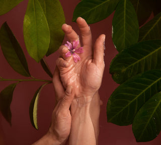 Hands holding a pink flower with green leaves, symbolising natural skincare, hydration, and gentle self-care