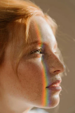  close-up of a woman’s freckled face with a soft rainbow light reflecting across her skin