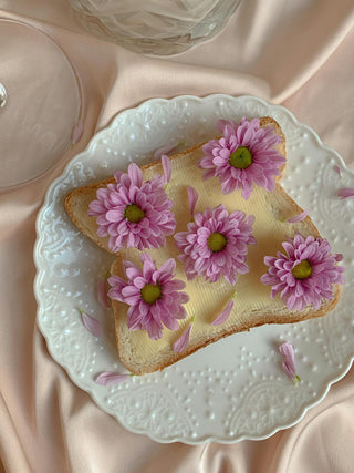 Aesthetic butter toast with pink flowers on a delicate vintage plate, styled on soft satin fabric. A dreamy, cottagecore-inspired food arrangement perfect for romantic breakfast ideas or floral food photography