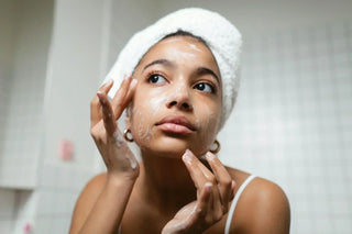 Woman with a towel headwrap applying a creamy facial cleanser, promoting gentle skincare and hydration